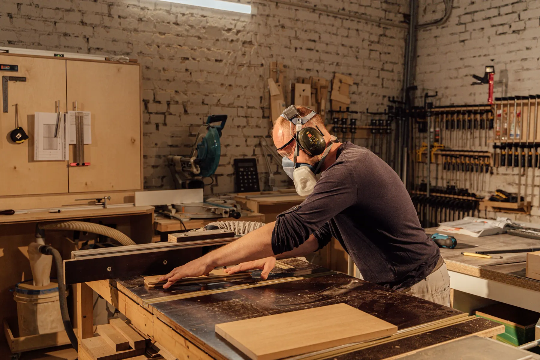 Cabinetmaker at a table saw in a workshop, wearing a mask and ear defenders